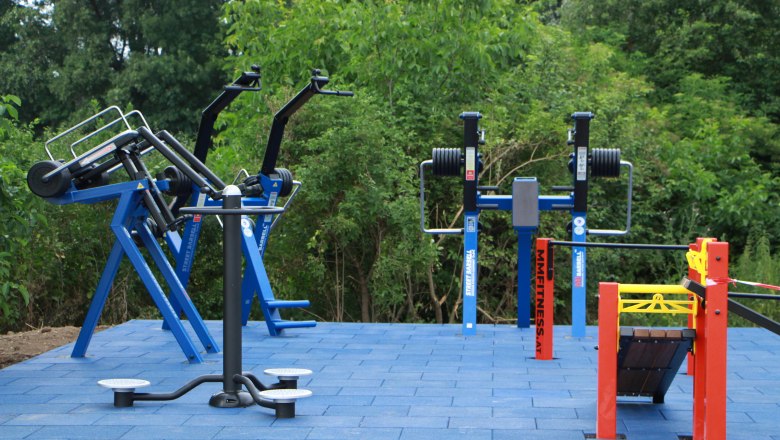 Outdoor-Fitnessgeräte auf blauen Bodenplatten im Freien.
