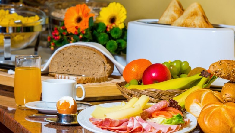 Frühstücksbuffet mit Brot, Aufschnitt, Käse, Obst, Brötchen, Saft und Ei.