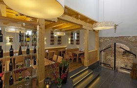 Innenansicht eines Heurigen mit Holzmöbeln, Weinregal und dekorativen Lampen.