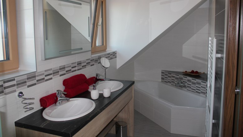 Modernes Badezimmer mit Doppelwaschbecken, Badewanne und roten Handtüchern.