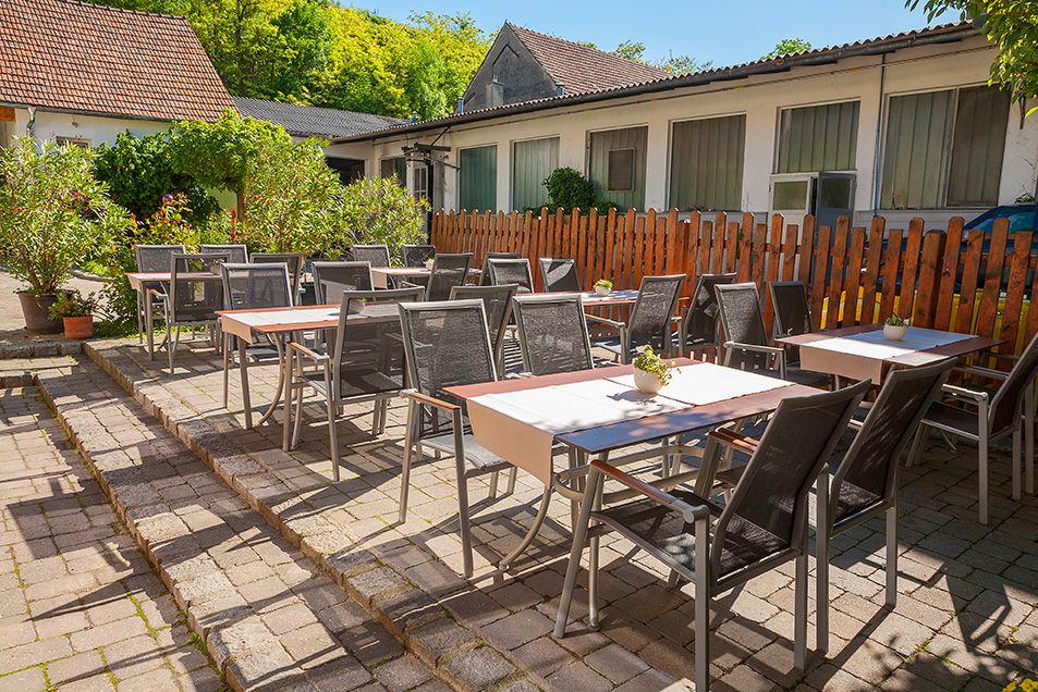 Gastgarten mit Tischen und Stühlen im Freien, umgeben von Pflanzen und einem Holzzaun.