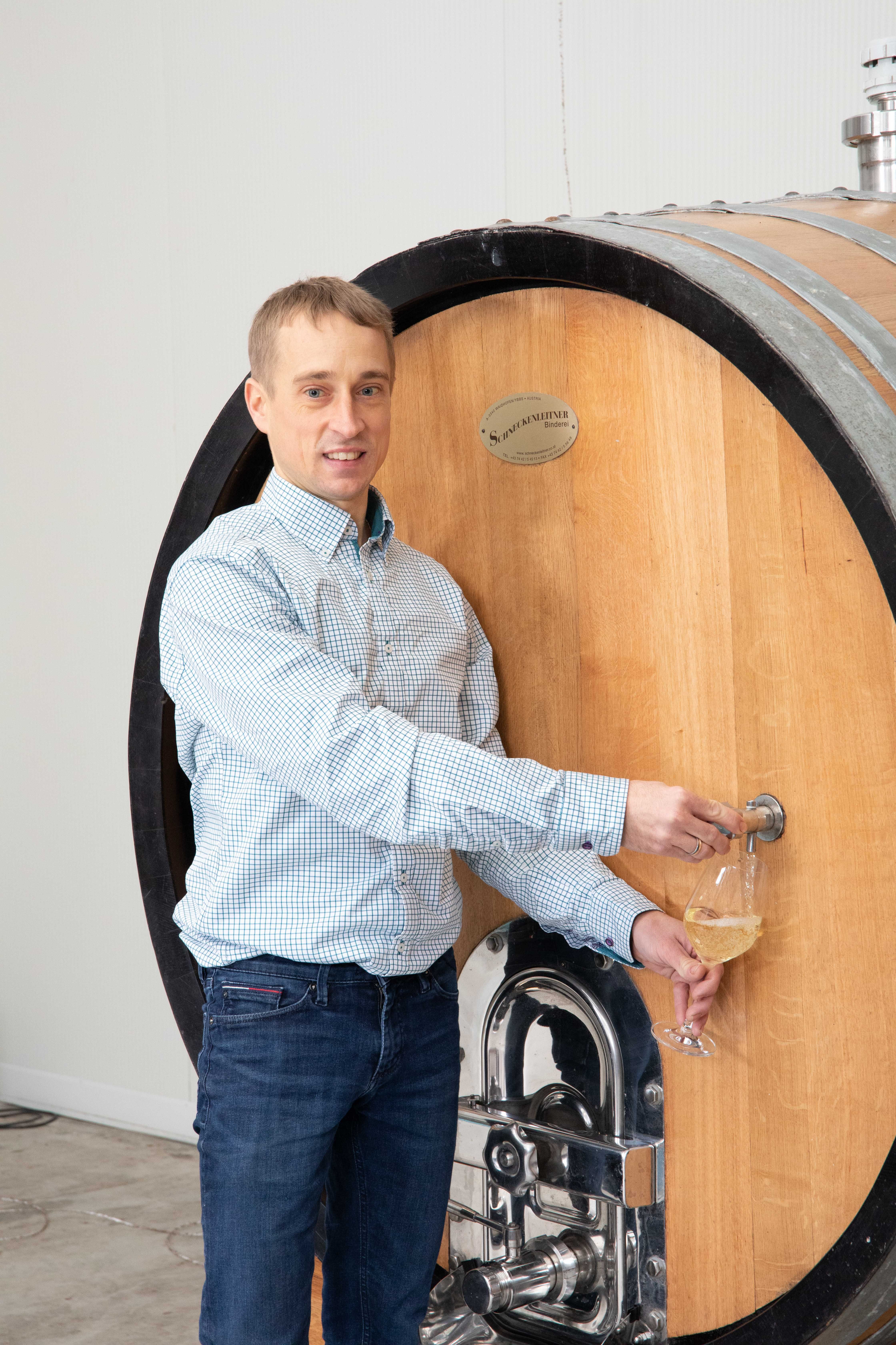 Person draws wine from a large wooden barrel into a glass.