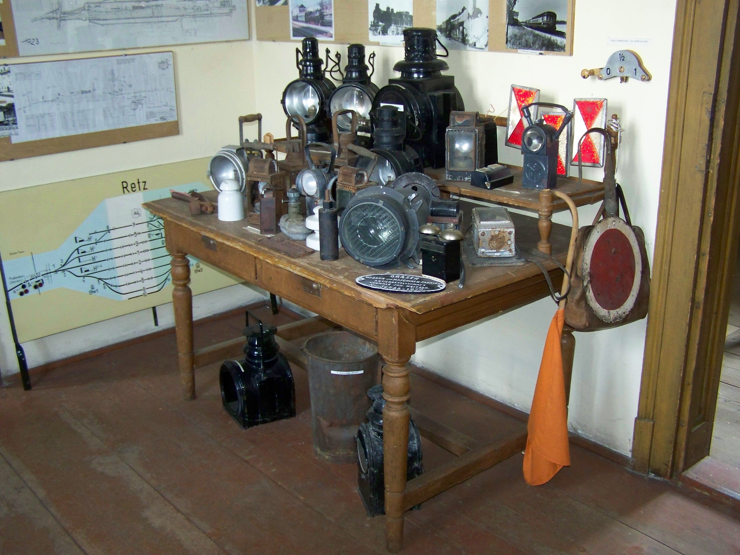 Ein Tisch mit alten Eisenbahnlampen und Signalen in einem Raum mit historischen Plänen an der Wand.