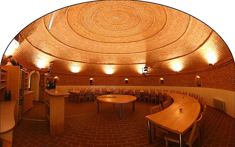 Interior view of a round wine cellar with brick walls and wooden furniture.