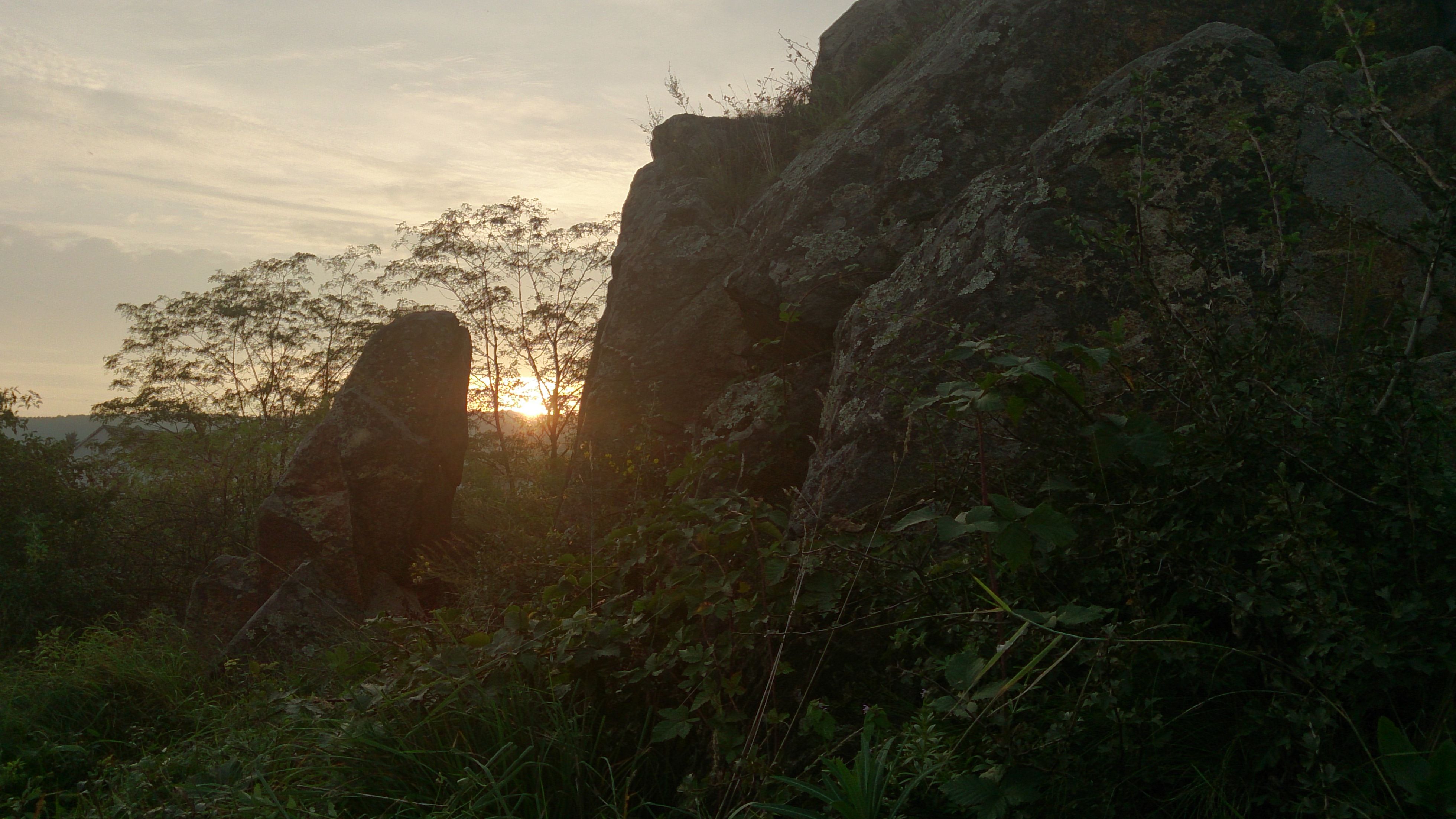 Sonnenuntergang hinter großen Felsen und Bäumen in einer natürlichen Umgebung.