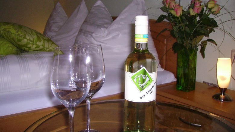 Ein gemütliches Gästezimmer mit einer Flasche Wein, zwei Gläsern und einem Blumenstrauß auf einem Tisch.