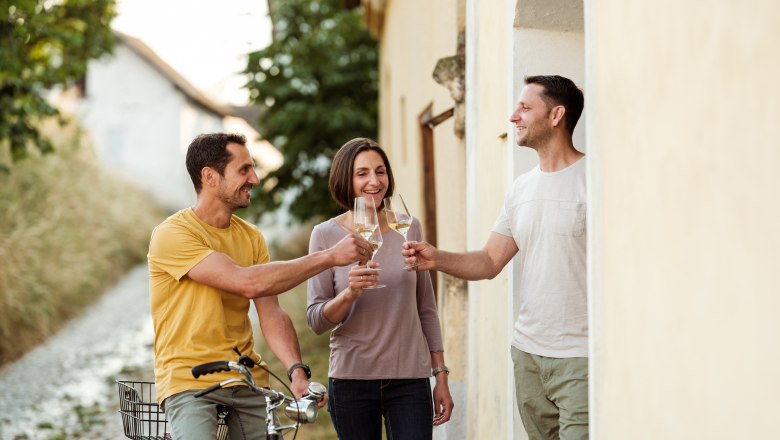Three people clink glasses of wine, one person sits on a bicycle.