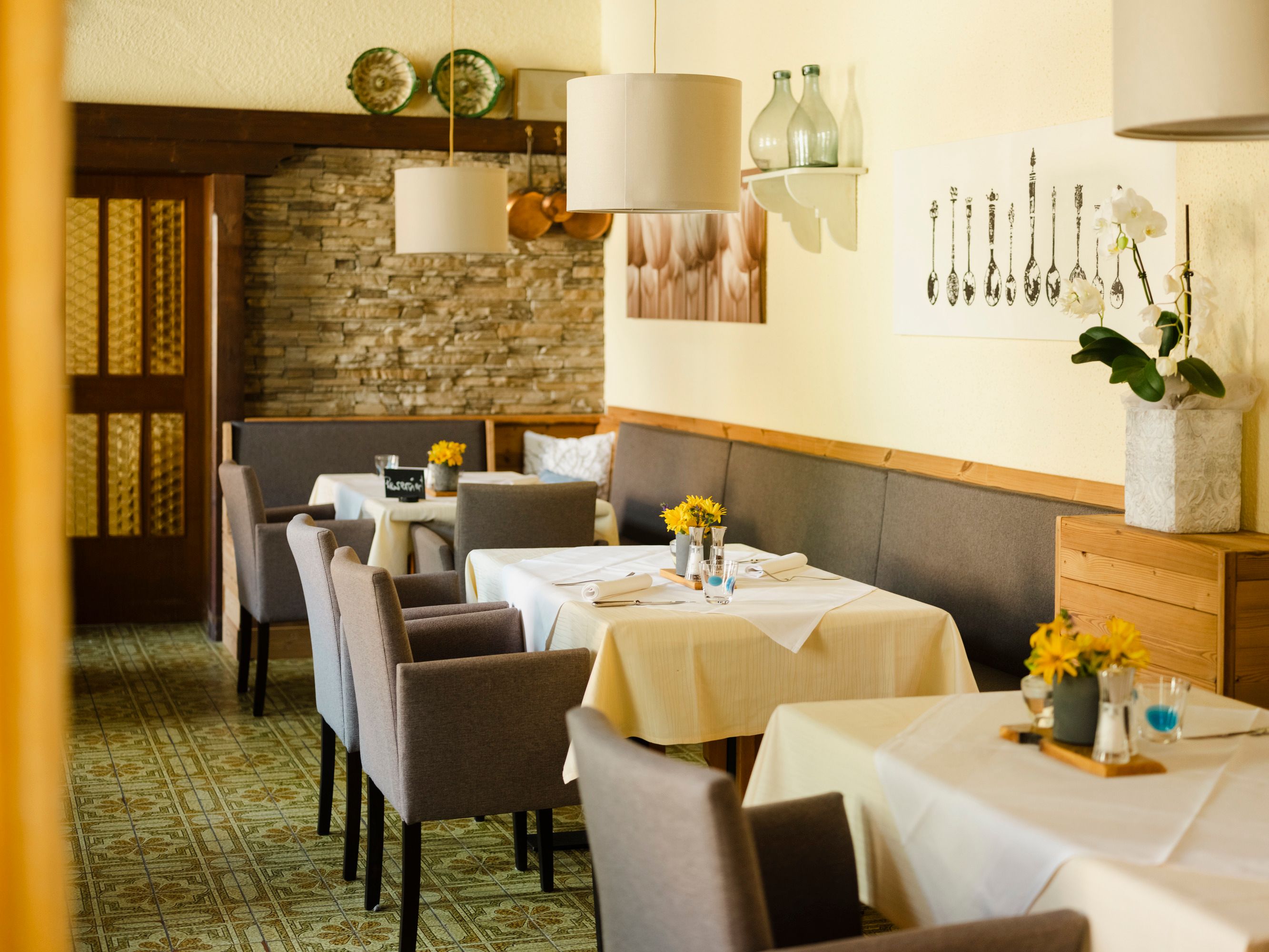 Einladendes Restaurant mit gedeckten Tischen, grauen Stühlen und dekorativen Elementen an den Wänden.