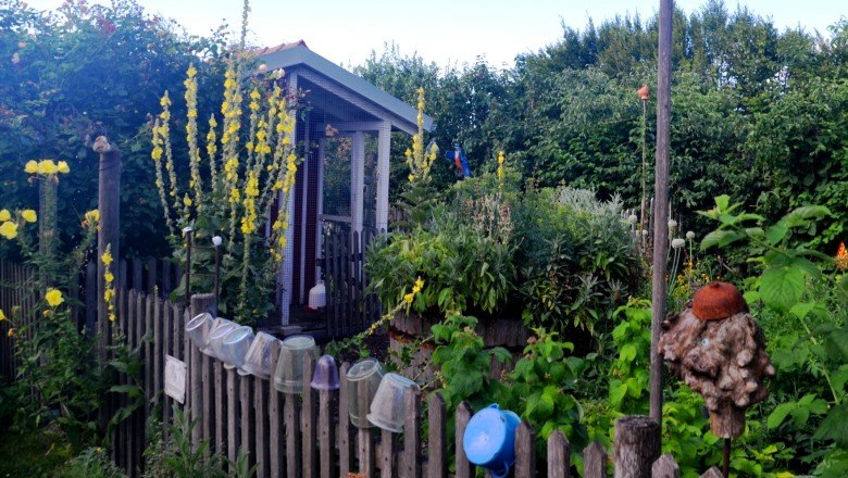 Ein kleiner Garten mit Hochbeet, umgeben von einem Holzzaun und blühenden Pflanzen.