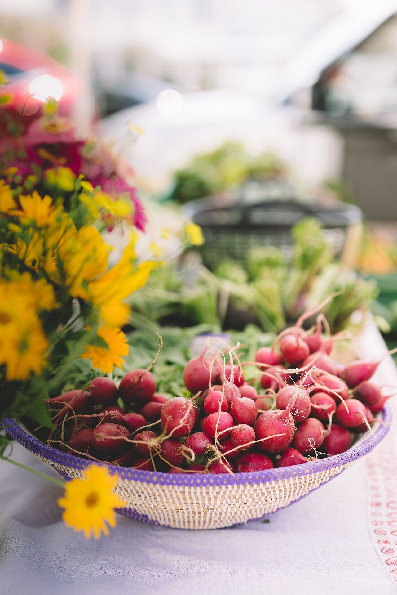 Frische Radieschen in leuchtendem Rot liegen einladend in einem geflochtenen Korb, umgeben von bunten Blumen. Der Duft von frischem Gemüse und die lebendige Atmosphäre des Marktes laden dazu ein, die kulinarischen Köstlichkeiten der Region zu entdecken.