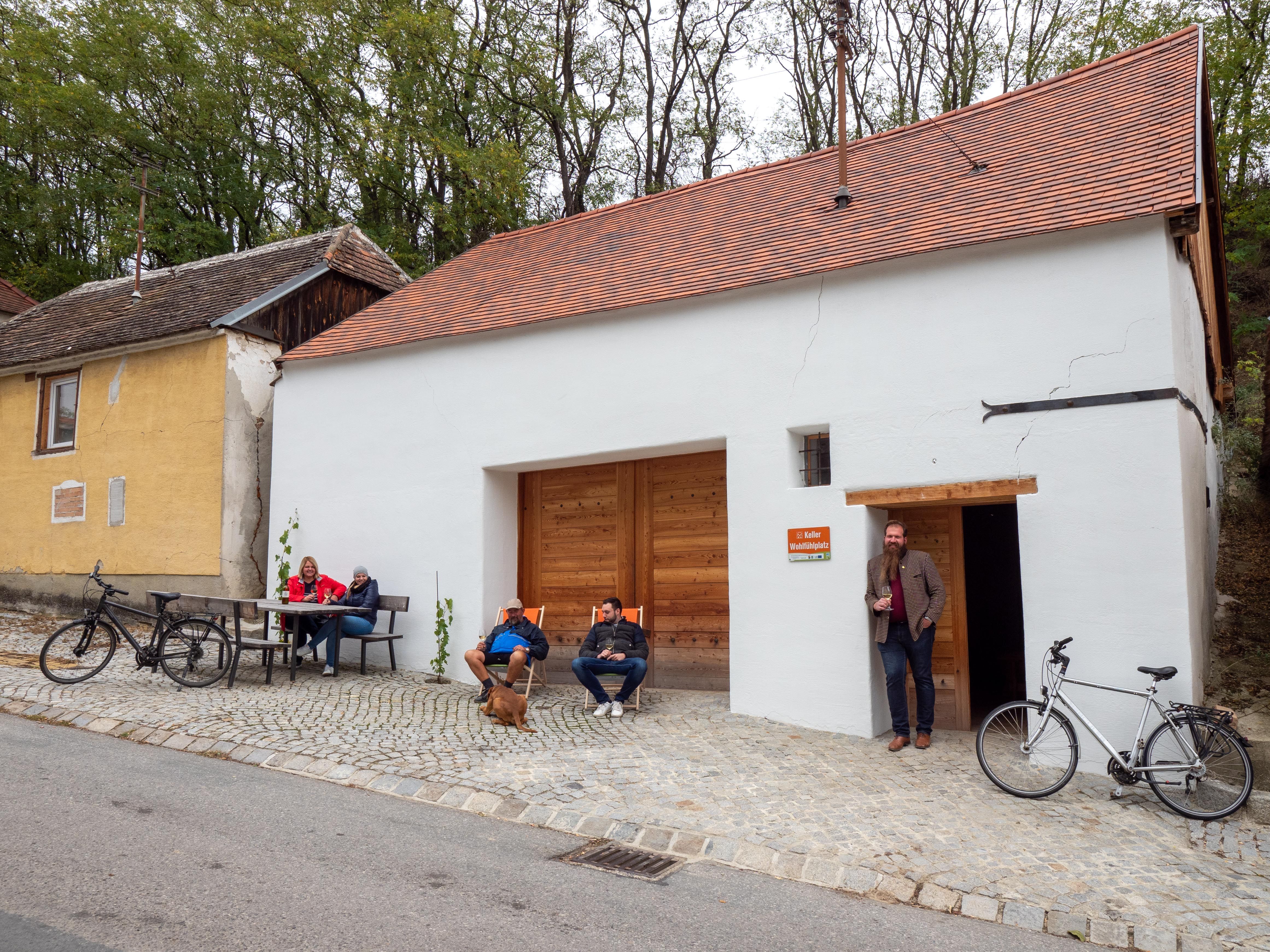Menschen sitzen vor einem Kellergebäude mit Fahrrädern.