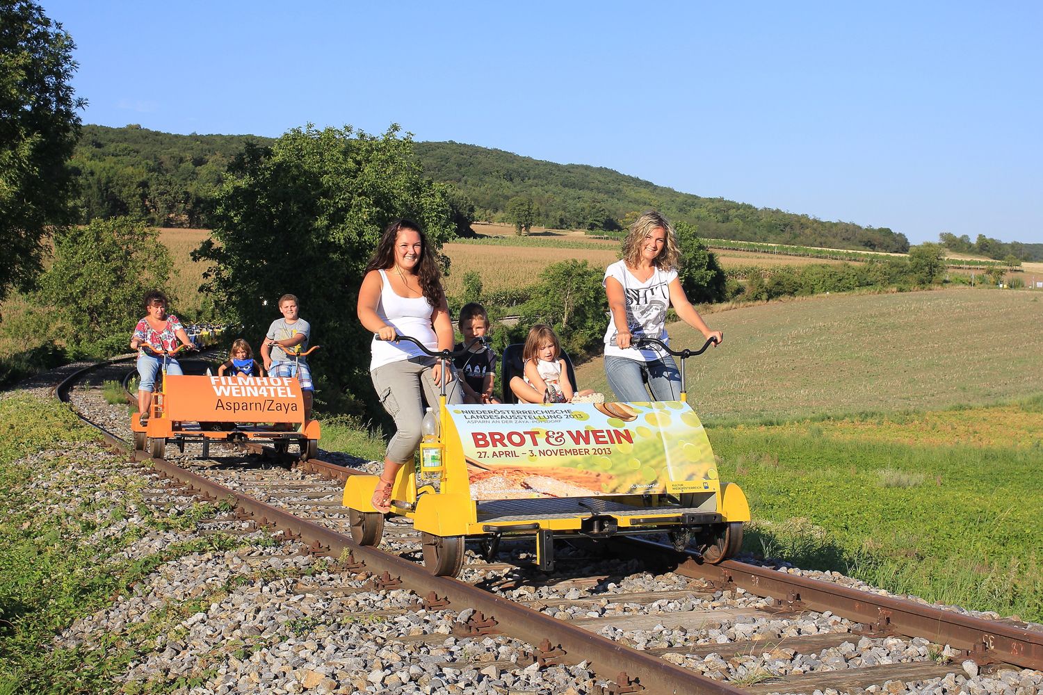Menschen fahren auf einer Draisine durch eine ländliche Landschaft.