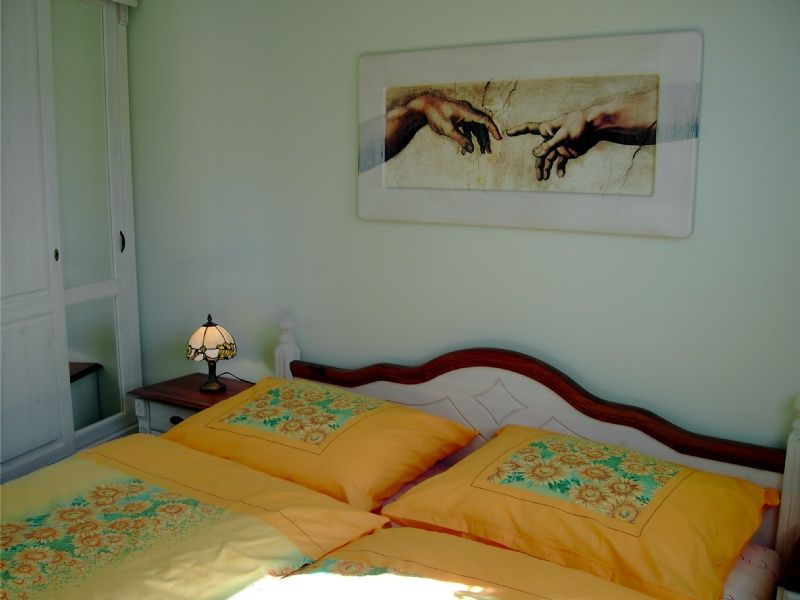 Gästezimmer mit gelber Bettwäsche, Nachttischlampe und Wandbild der Erschaffung Adams.