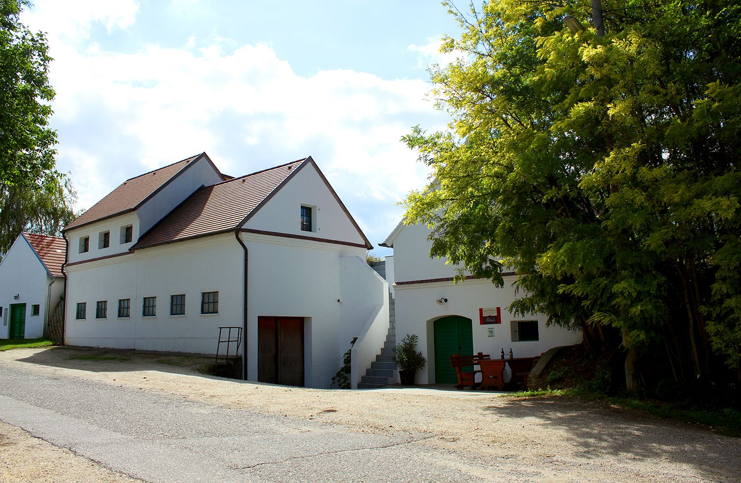 White building with a red roof and green doors, surrounded by trees.