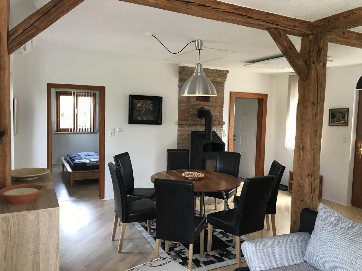 Essbereich mit rundem Holztisch, schwarzen Stühlen und Holzofen in einem Raum mit Holzbalken.