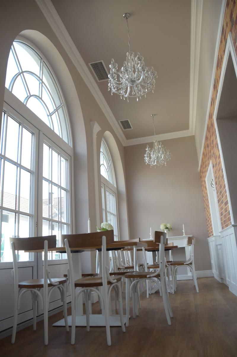 Eleganter Raum mit hohen Fenstern, Kronleuchtern und Holzmöbeln.