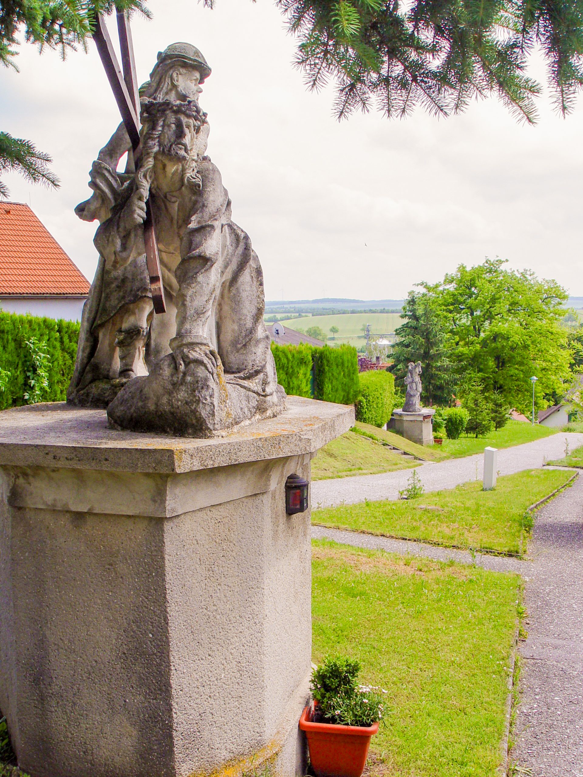 Steinstatue auf einem Sockel mit grüner Landschaft im Hintergrund.