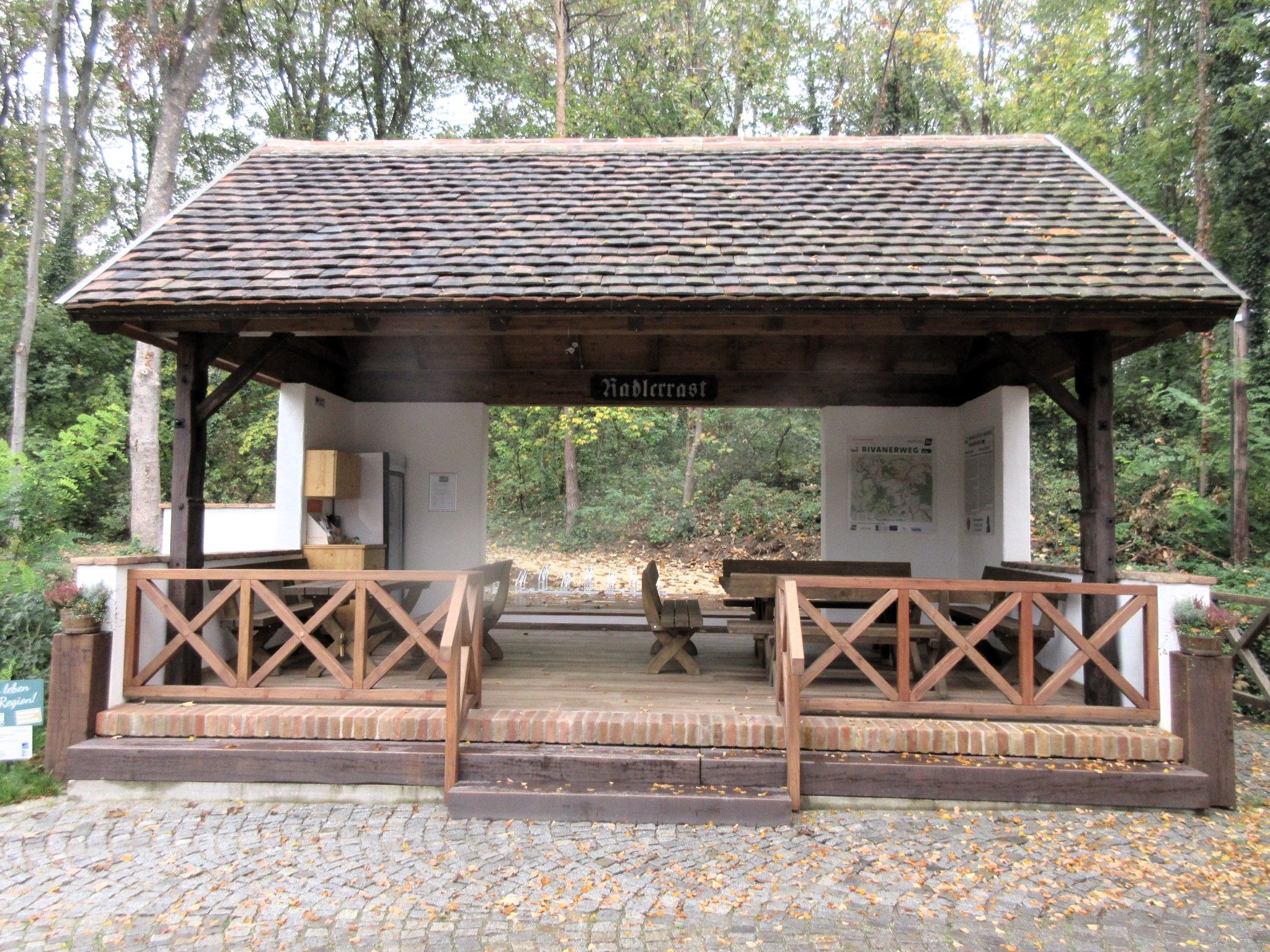 Überdachte Raststation für Radfahrer im Wald mit Sitzgelegenheiten und Informationsschildern.