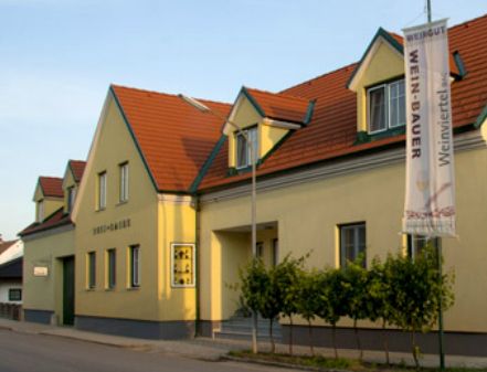 Žlutá budova vinařství s červenou střechou a vlajkou.