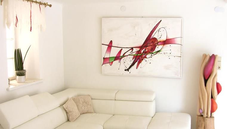 Modernes Wohnzimmer mit weißem Sofa, abstraktem Kunstwerk an der Wand und dekorativer Pflanze.