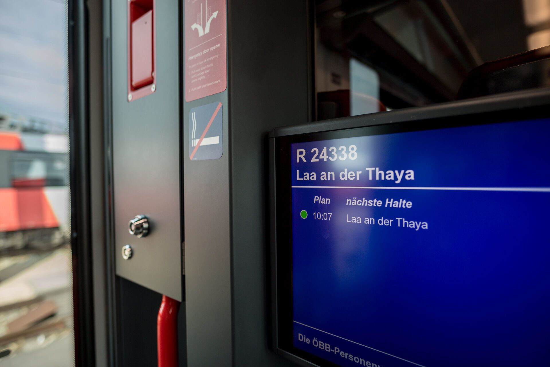 Die sanften Bewegungen des Zuges laden dazu ein, die vorbeiziehende Landschaft zu genießen. Ein digitales Display zeigt die nächste Haltestelle an, während die Vorfreude auf neue Abenteuer in der Luft liegt. Die gemütliche Atmosphäre im Inneren des Wagens verspricht eine entspannte Reise.