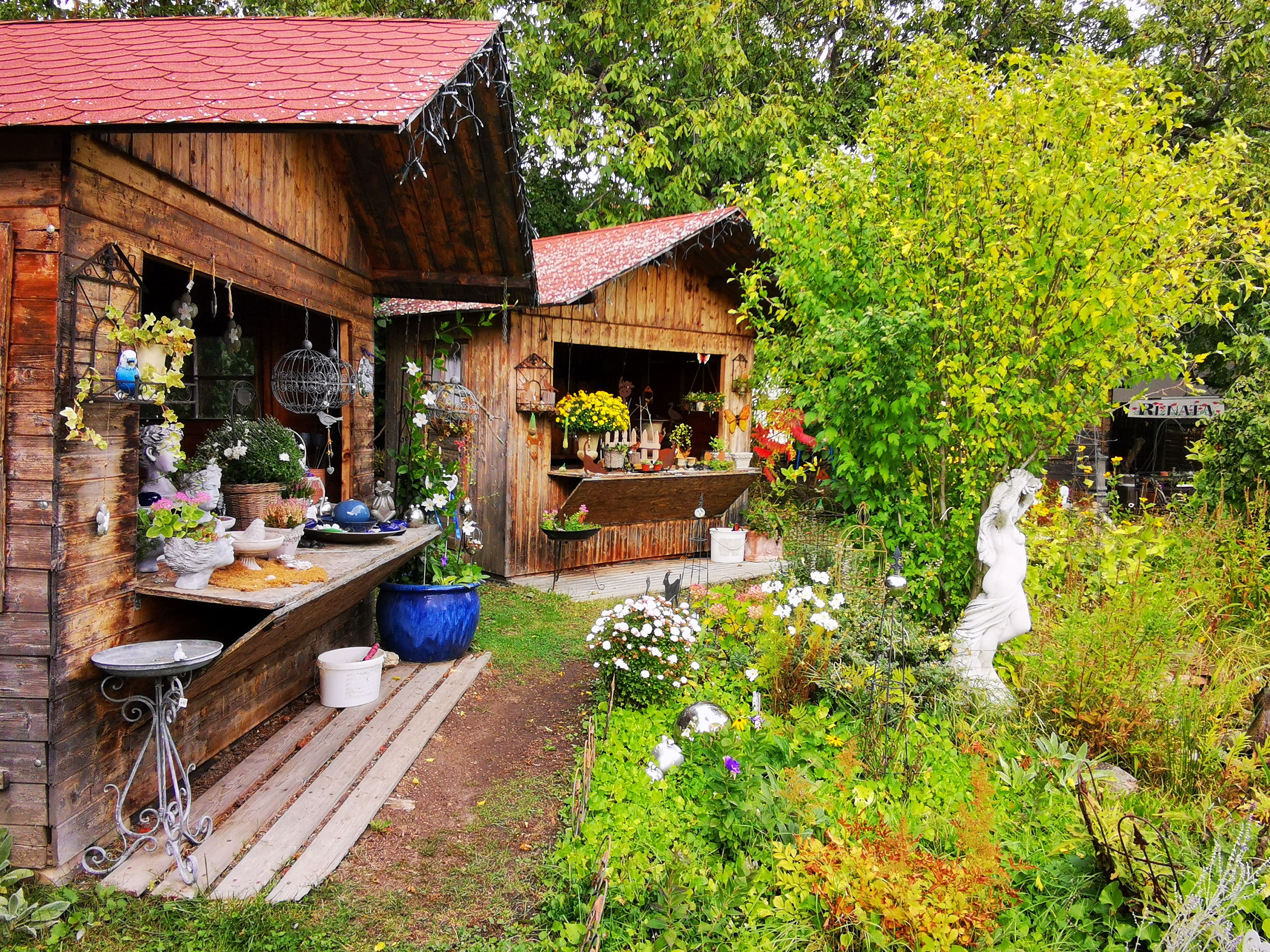 Garten mit Holzhütten, Pflanzen und Keramikdekorationen.