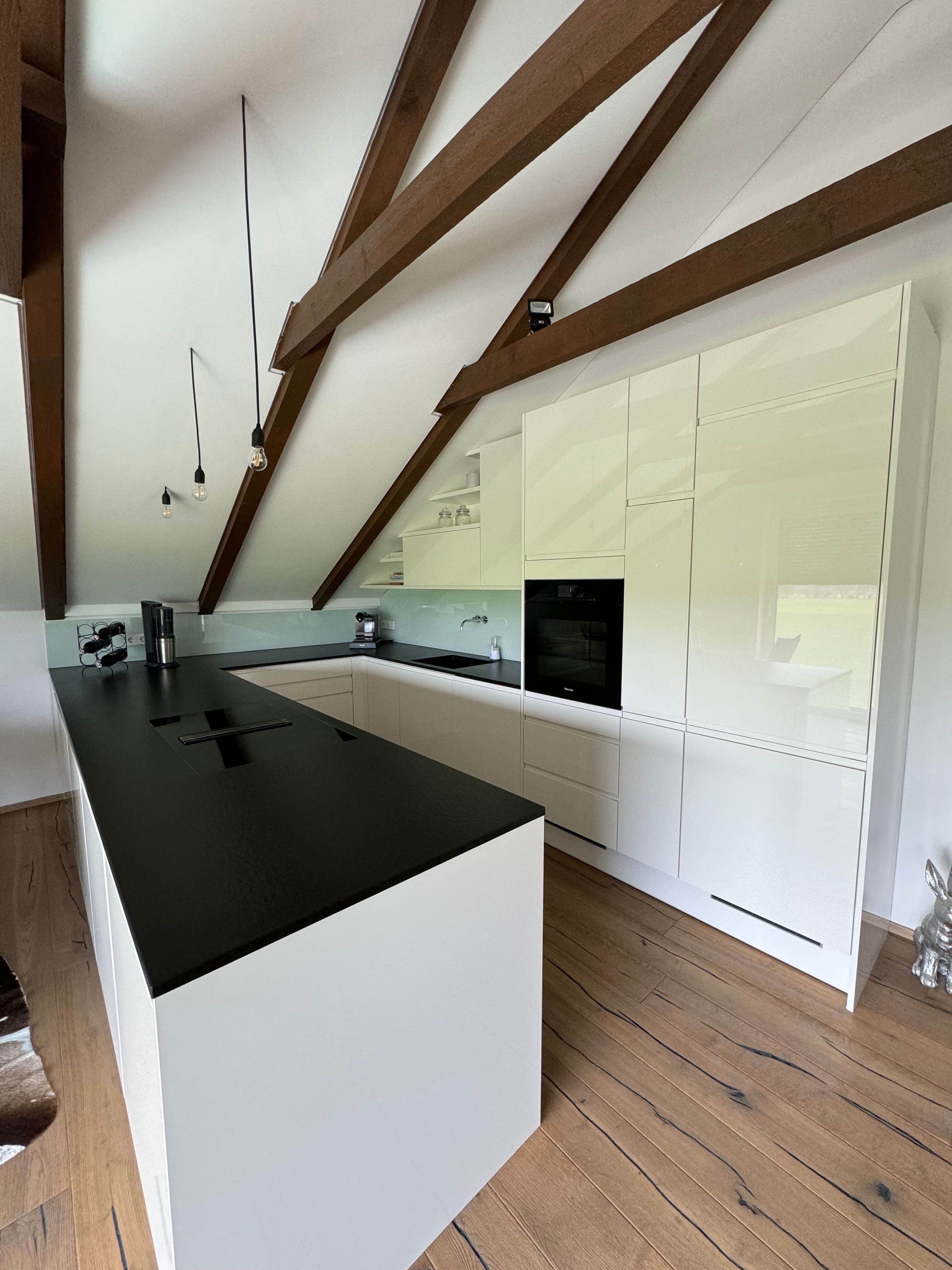 Moderne Küche mit weißen Schränken, schwarzer Arbeitsplatte und Holzbalken an der Decke.