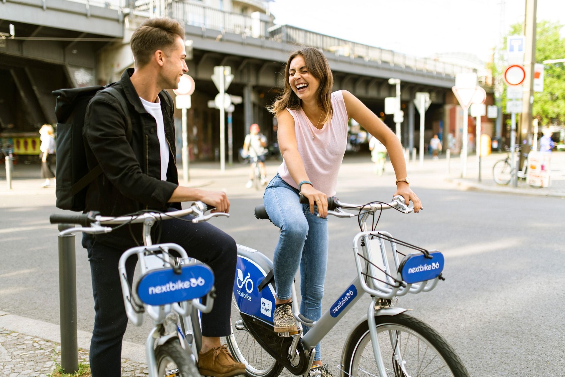 Zwei Personen lachen und sitzen auf Nextbike-Fahrrädern an einer Straßenecke.