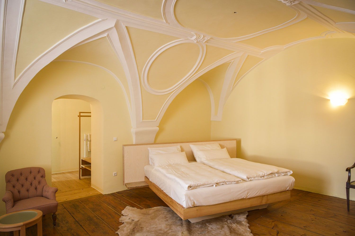 Ein elegantes Schlafzimmer mit gewölbter Decke, einem Doppelbett, einem Sessel und Holzboden.
