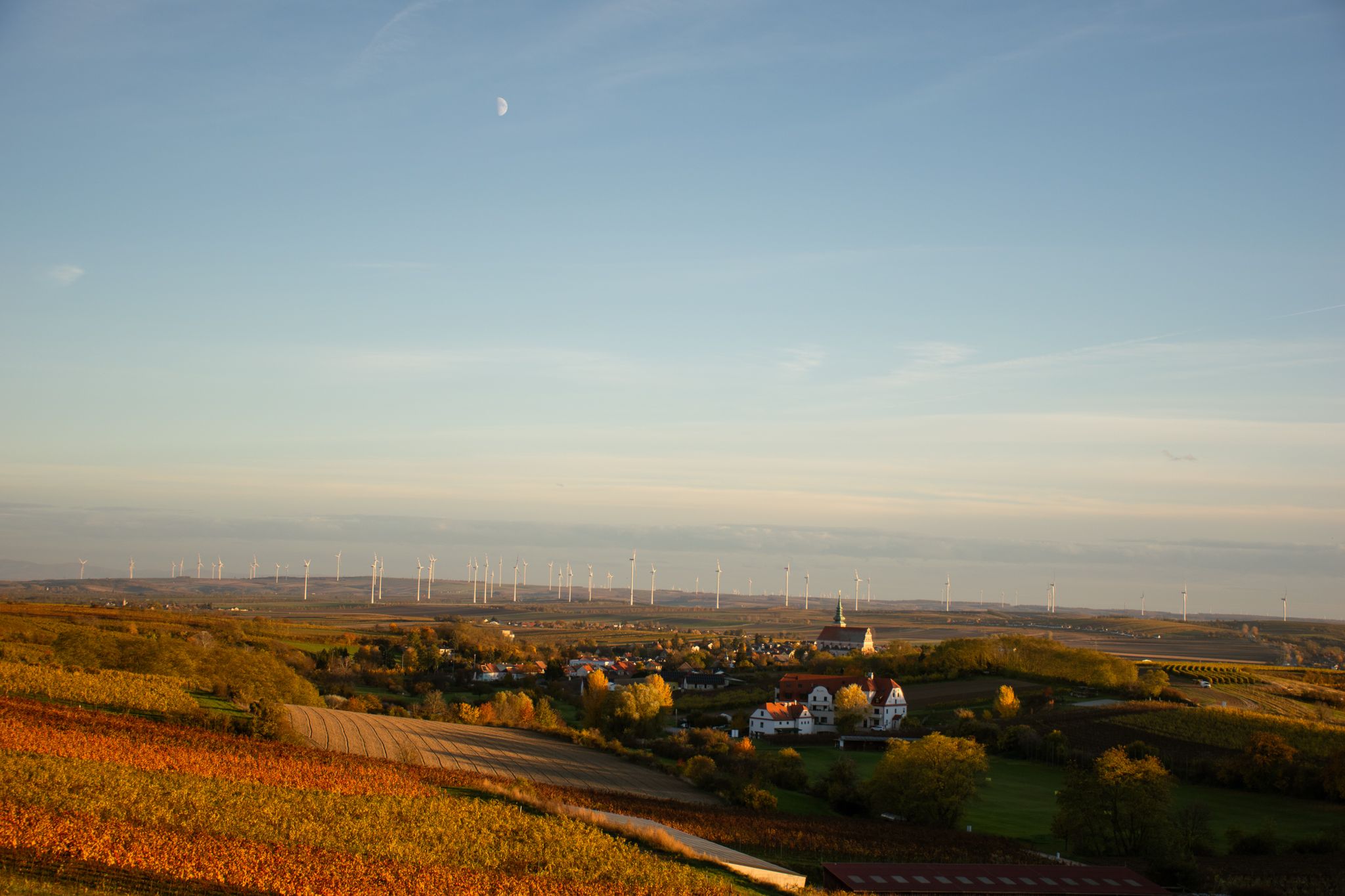 Landschaft mit Windrädern und Dorf im Vordergrund bei Sonnenuntergang.