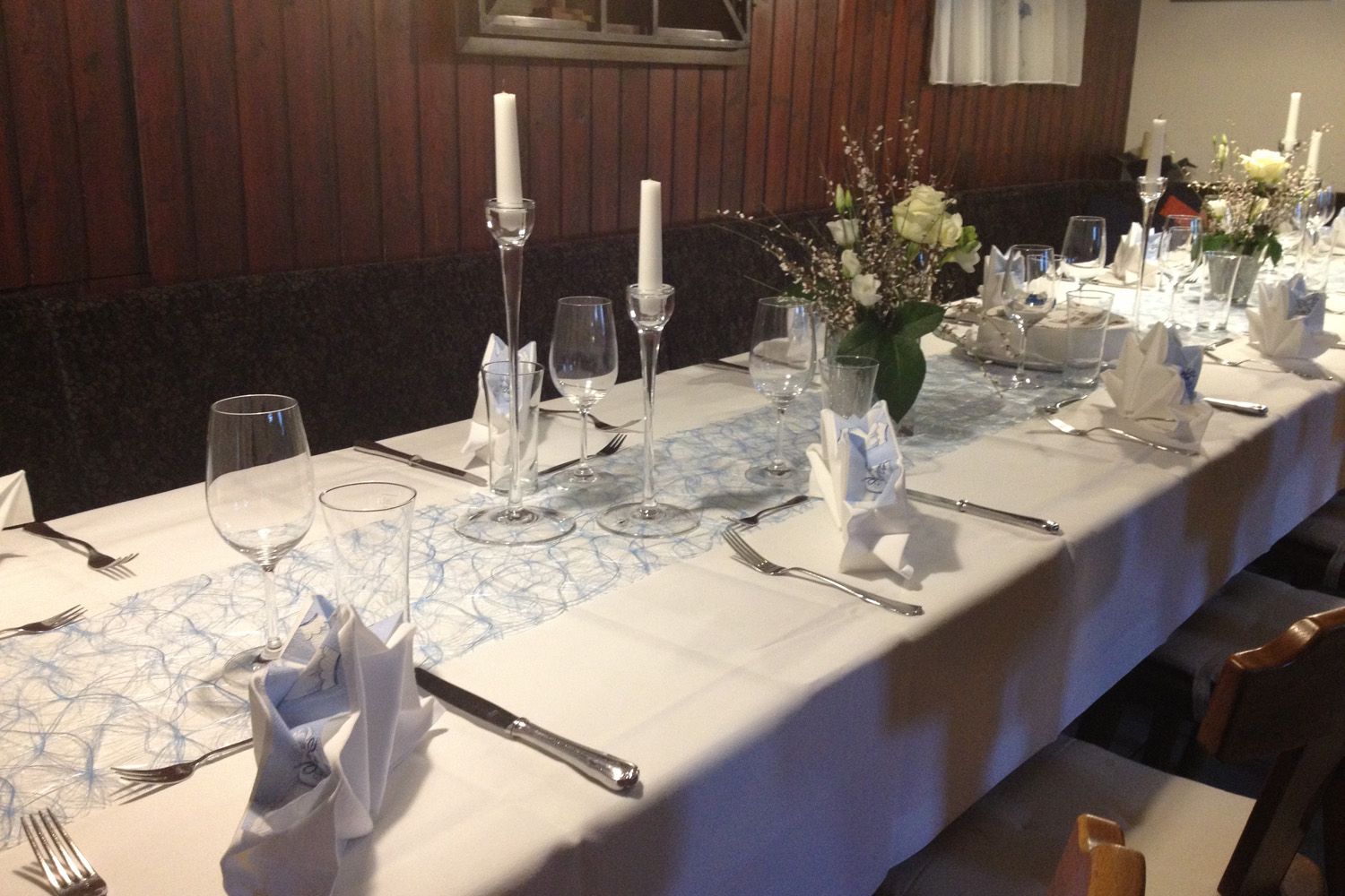 Elegante, festlich gedeckte Tafel mit weißen Tischdecken, Kerzen und Blumenarrangements.