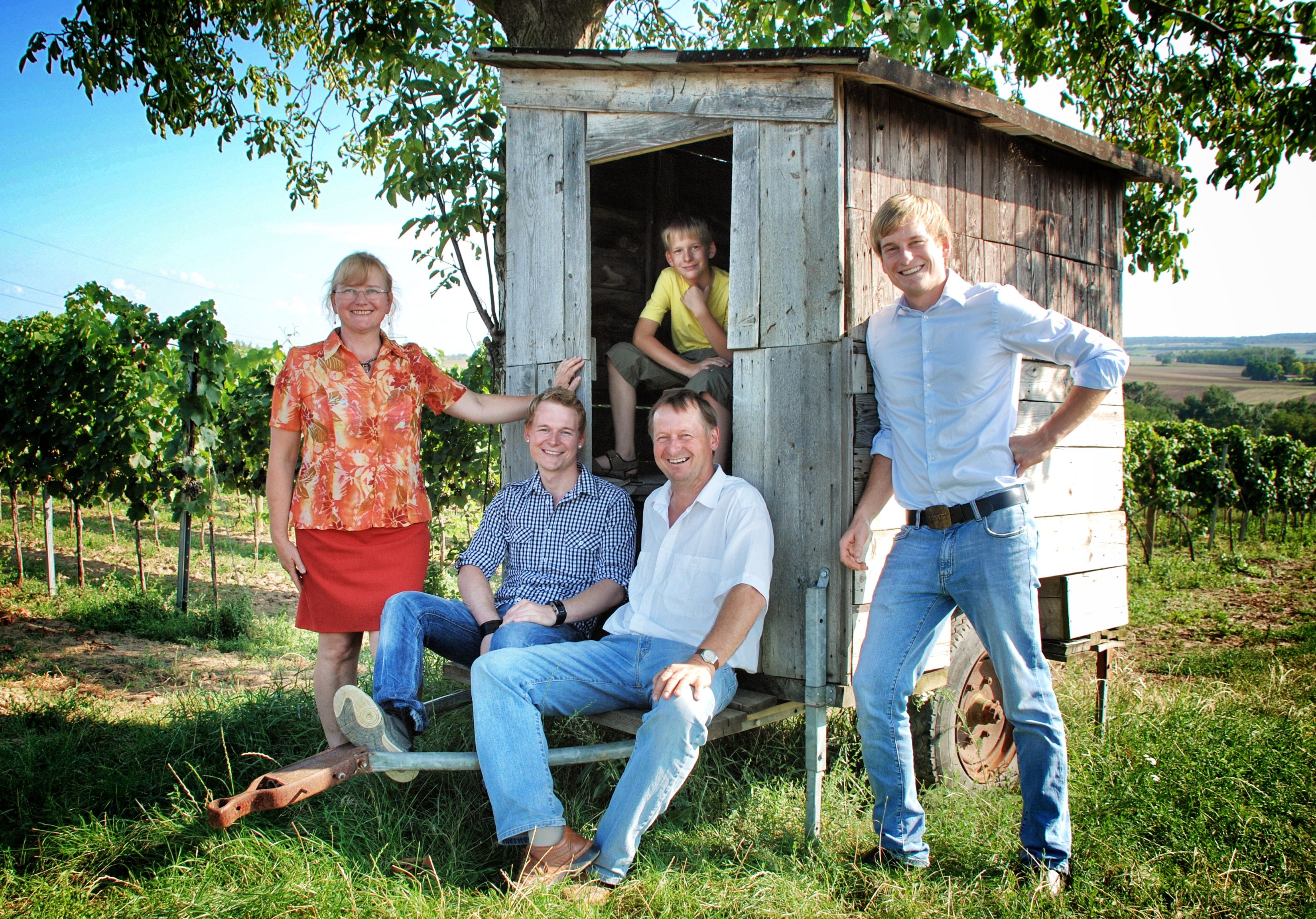 Eine Familie posiert vor einem kleinen Holzwagen in einem Weinberg.