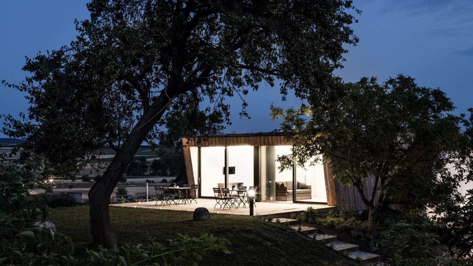 Modernes Gebäude mit Glasfront in ländlicher Umgebung bei Dämmerung.