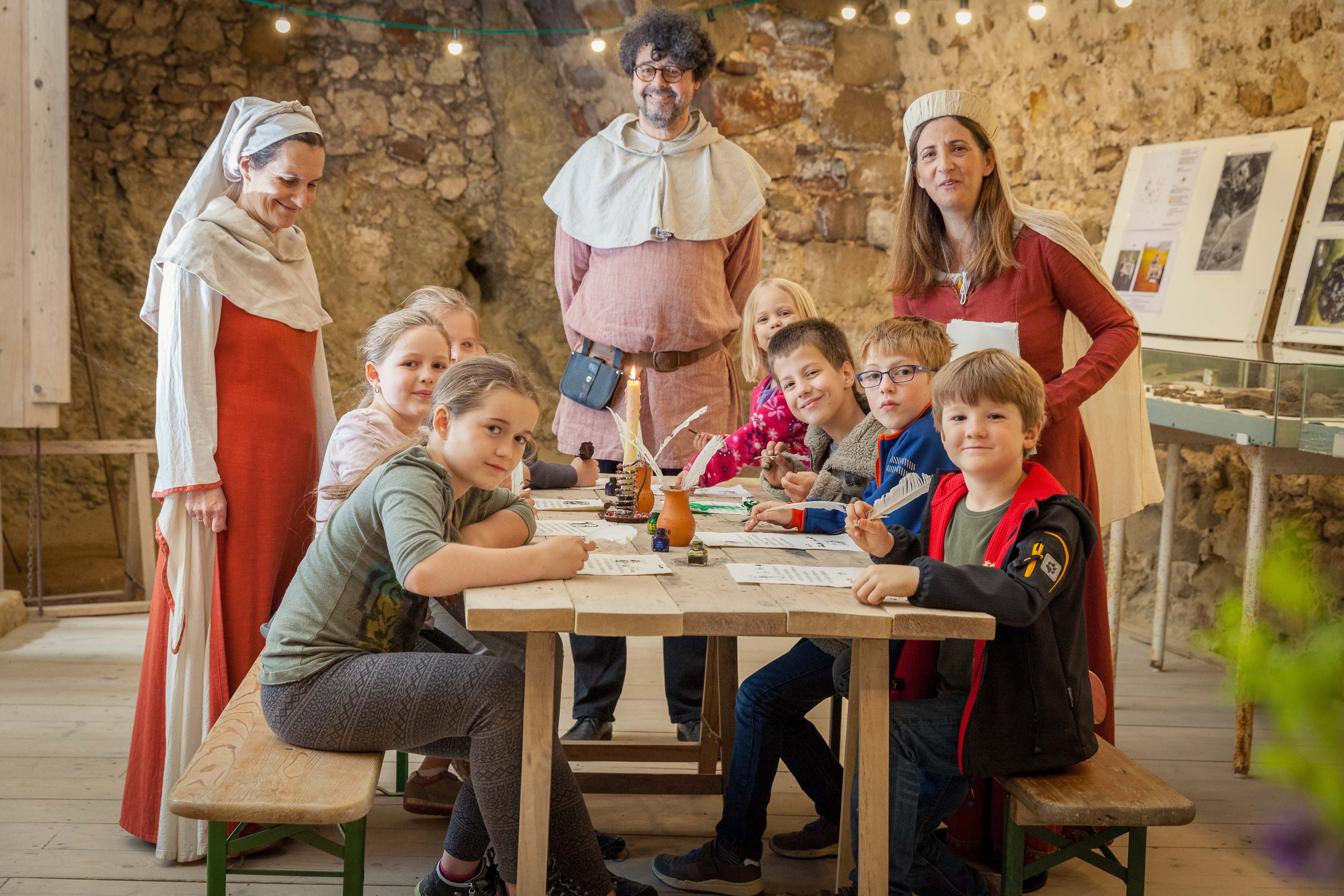 Kinder und Erwachsene in mittelalterlicher Kleidung an einem Tisch in einer Burgruine.