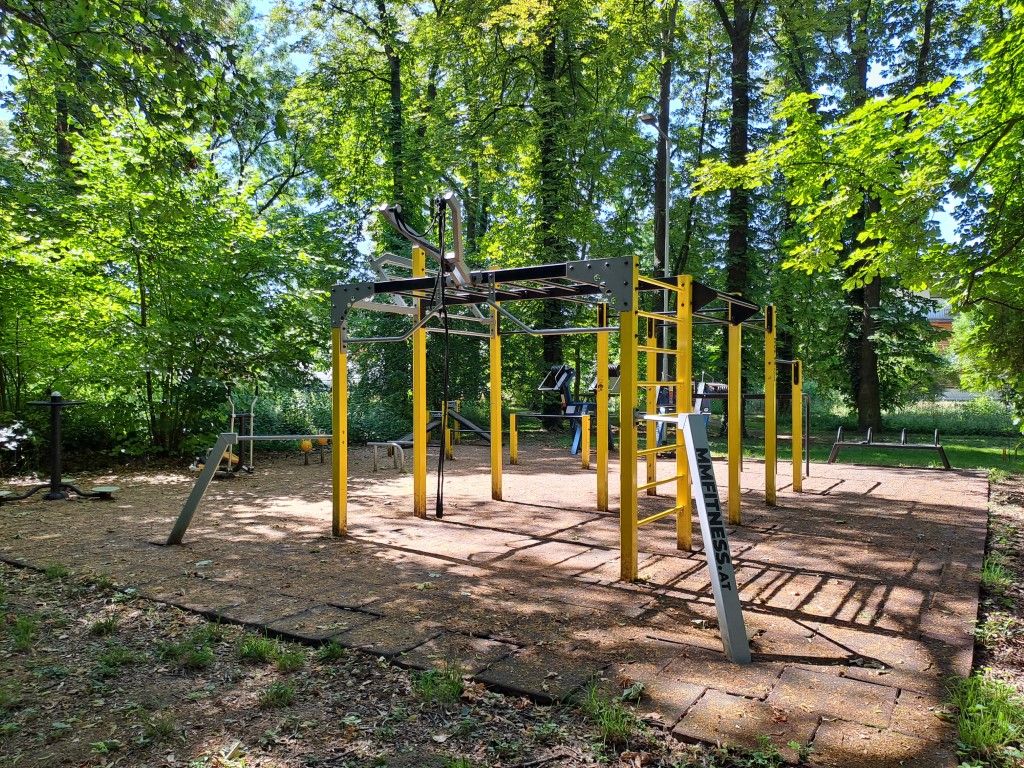 Calisthenics-Park im Freien mit gelben und grauen Klettergerüsten, umgeben von Bäumen.
