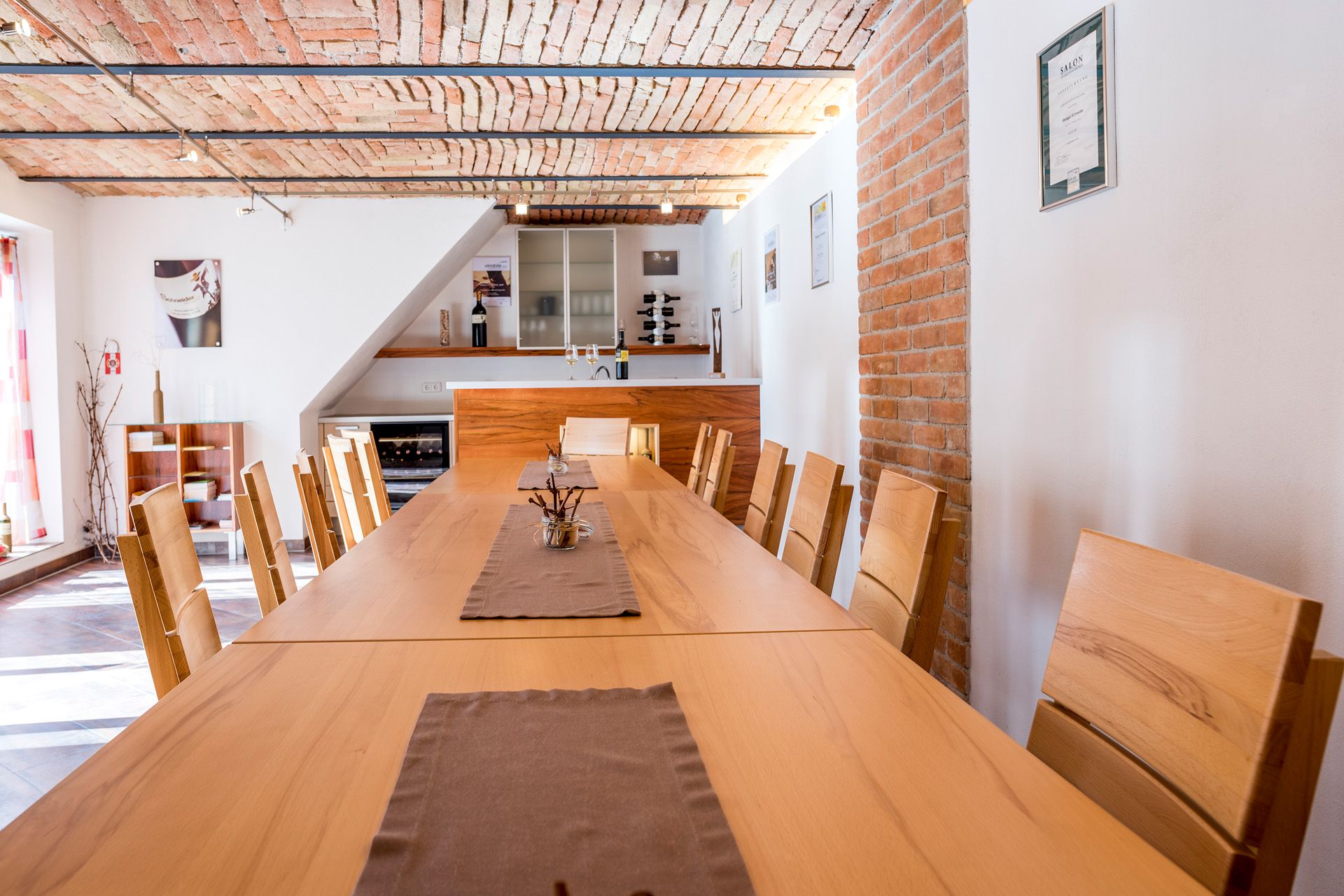 Verkostungsraum mit langem Holztisch und Stühlen, Ziegeldecke und Weinregal.