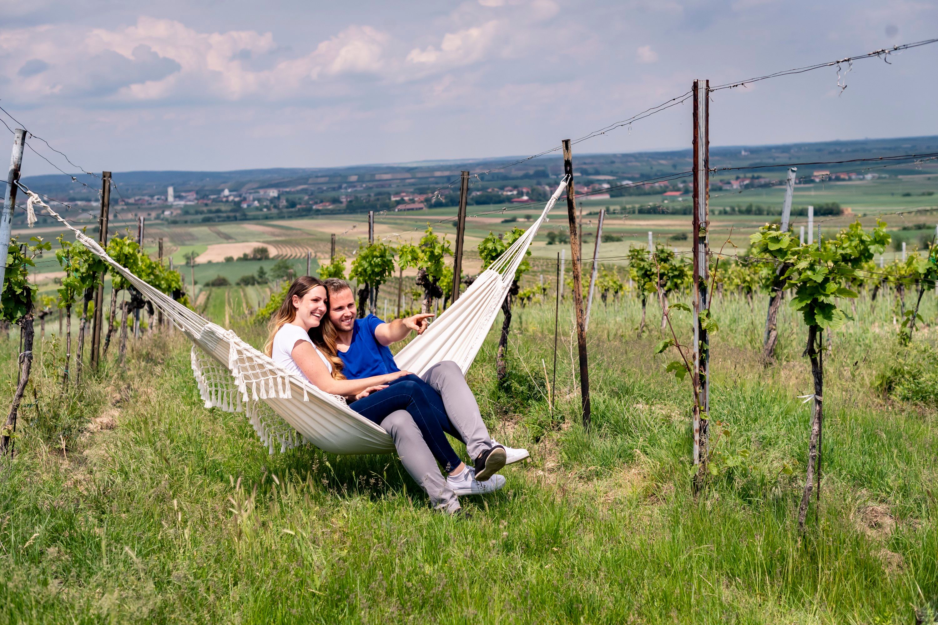 Ein Paar sitzt in einer Hängematte in einem Weinberg und genießt die Aussicht auf die Landschaft.