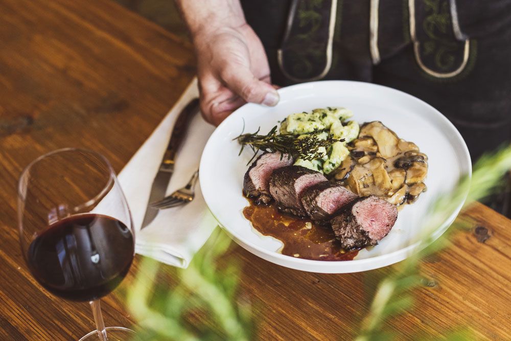 Ein Teller mit Fleisch, Pilzen und Spätzle, daneben ein Glas Rotwein.