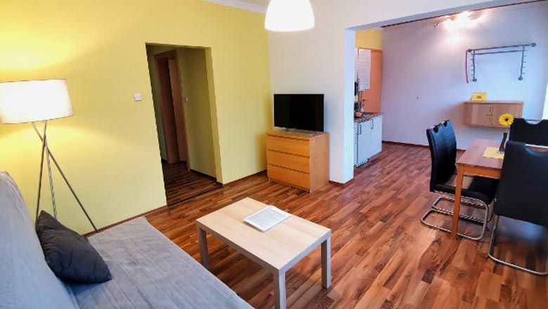 Modernes Wohnzimmer mit Holzboden, Sofa, Tisch, TV und Essbereich.