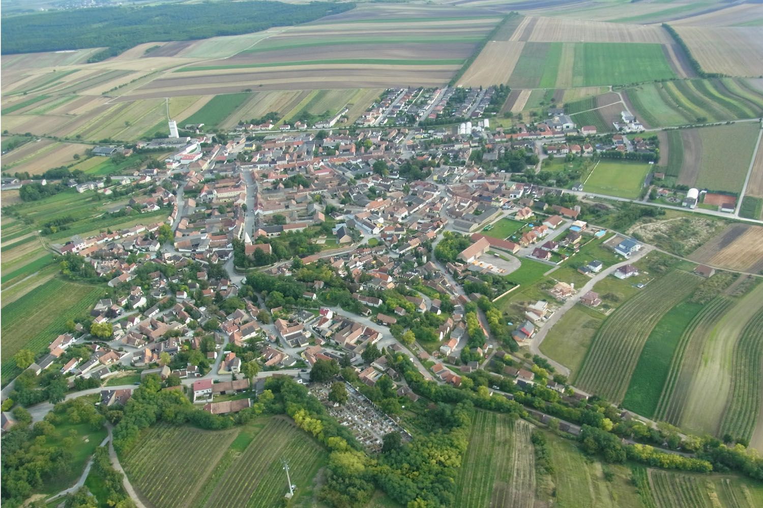 Luftaufnahme eines Dorfes mit umliegenden Feldern und Wäldern.