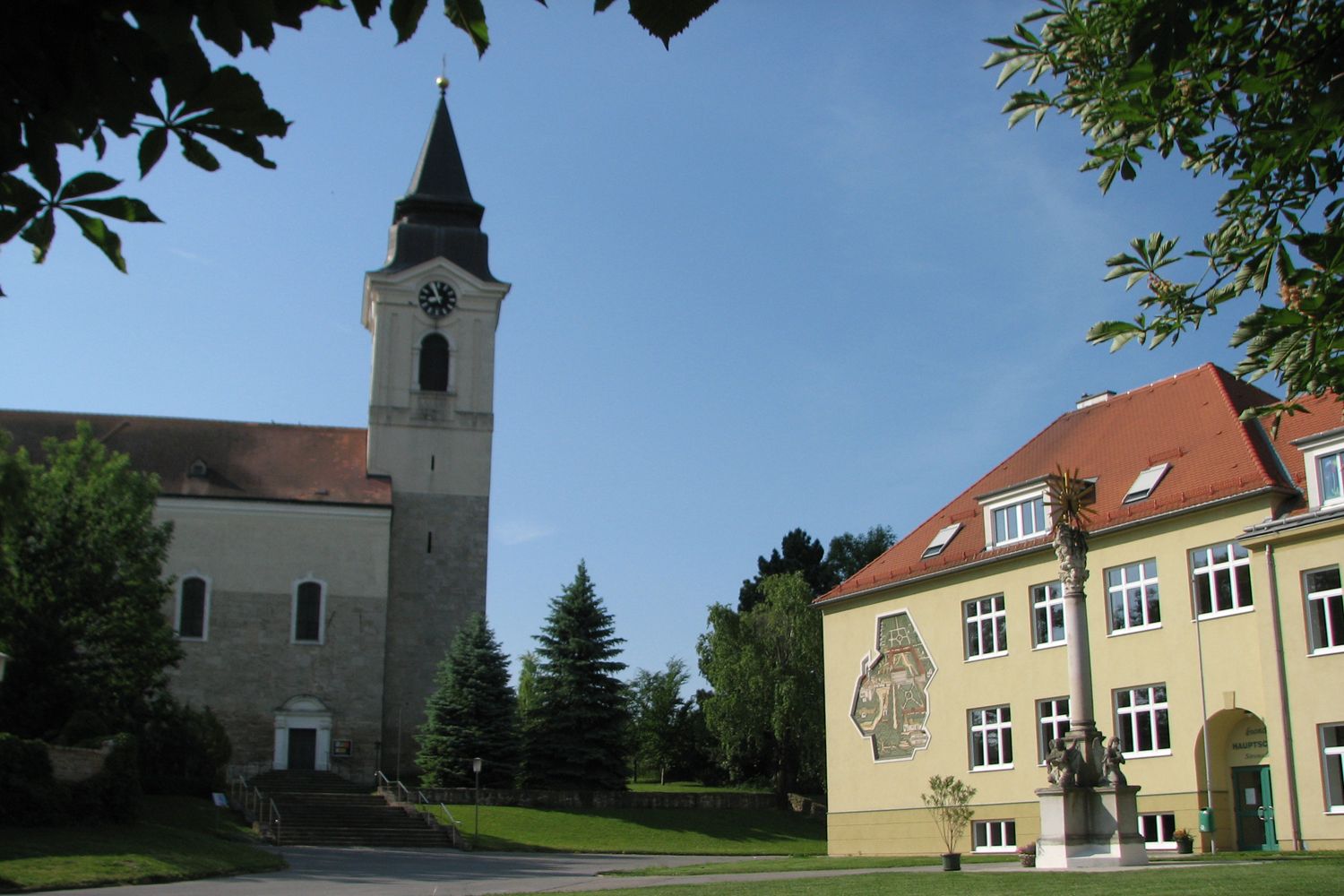 Kirche und Gebäude in Stronsdorf mit Uhrturm und Sonnenschein.