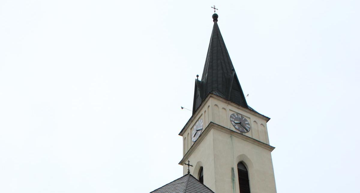 Kirchturm mit Uhr und spitzem Dach vor hellem Himmel.