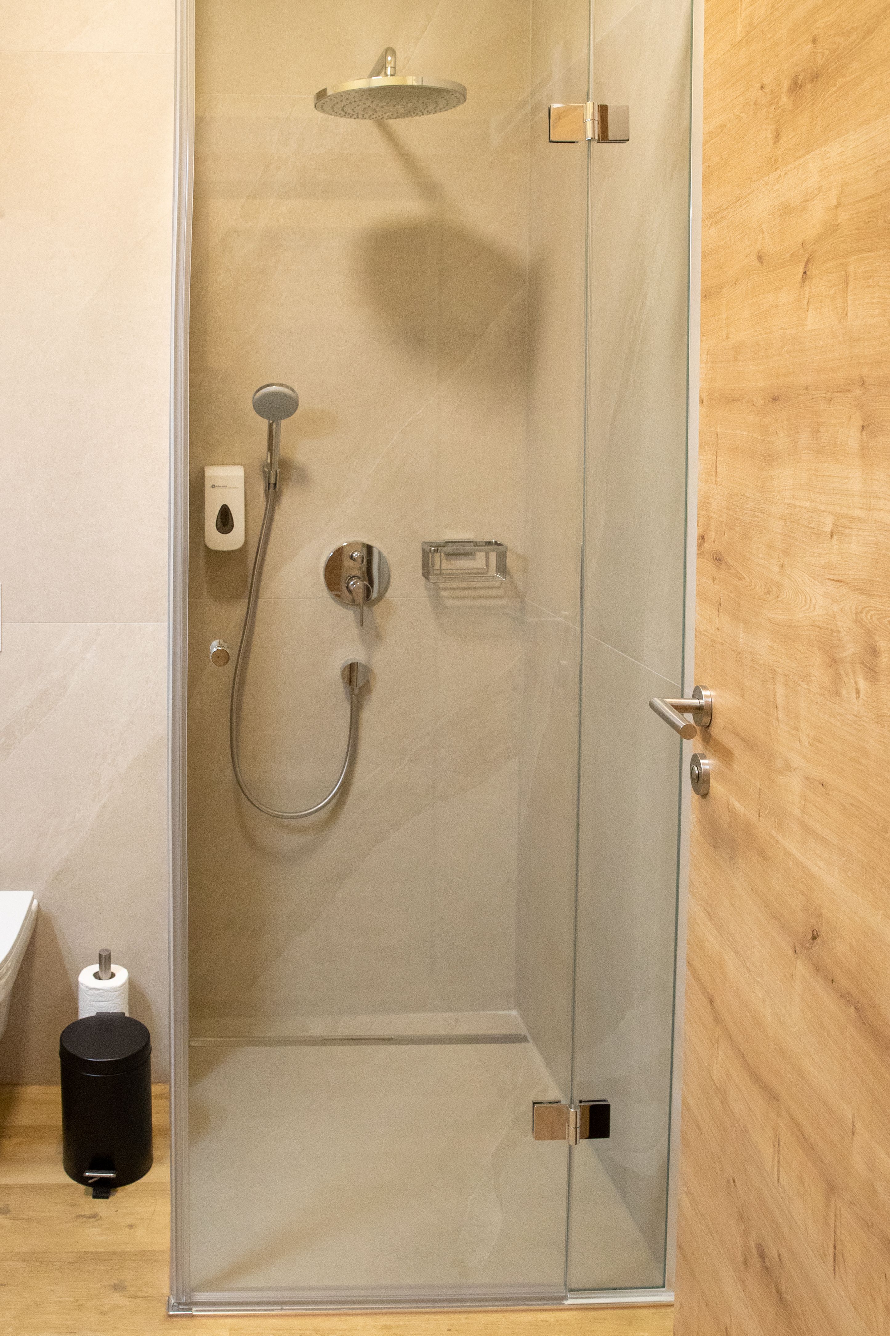 Modernes Badezimmer mit Glasdusche, Duschkopf und Holzdetails.