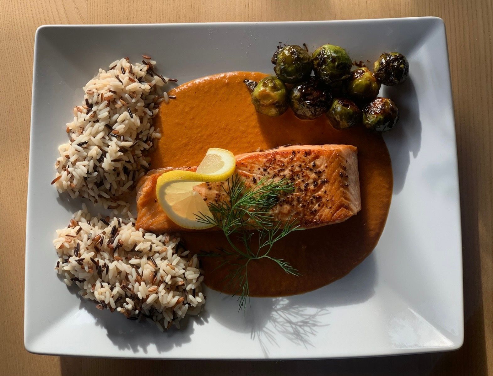 Ein Teller mit Lachsfilet auf roter Sauce, Wildreis und geröstetem Rosenkohl.