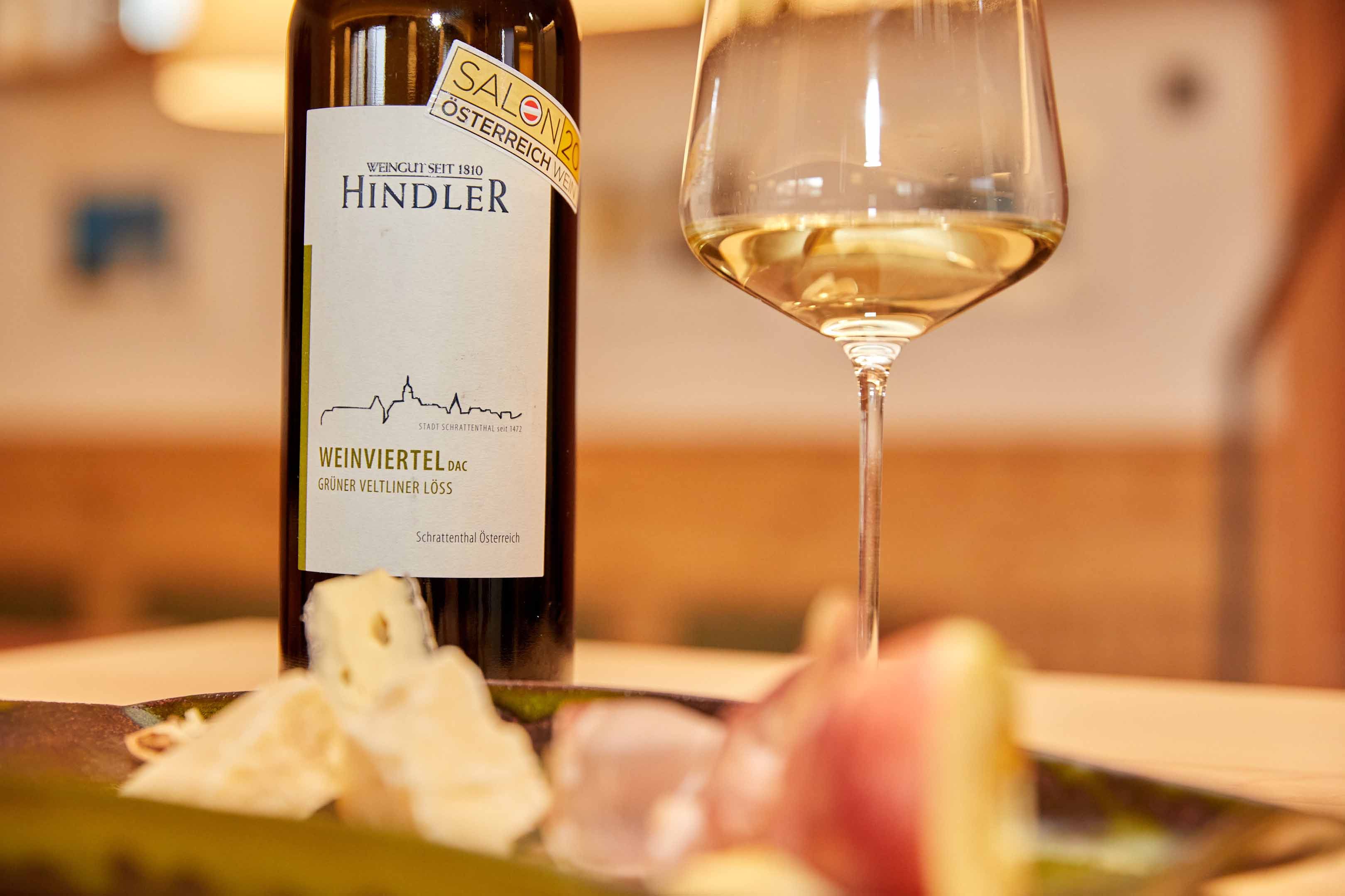 Weinflasche und Glas mit Weißwein, Käse und Schinken im Vordergrund.
