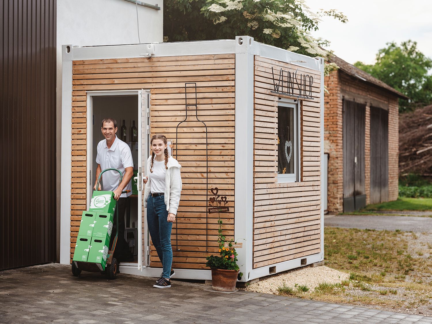 Two people in front of a small wooden building labeled 'Weinshop'.