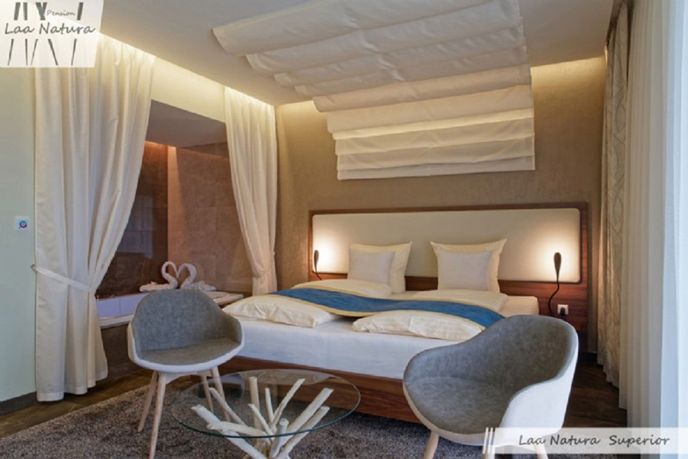 Modernes Doppelzimmer mit großem Bett, zwei grauen Stühlen und einem Glastisch.