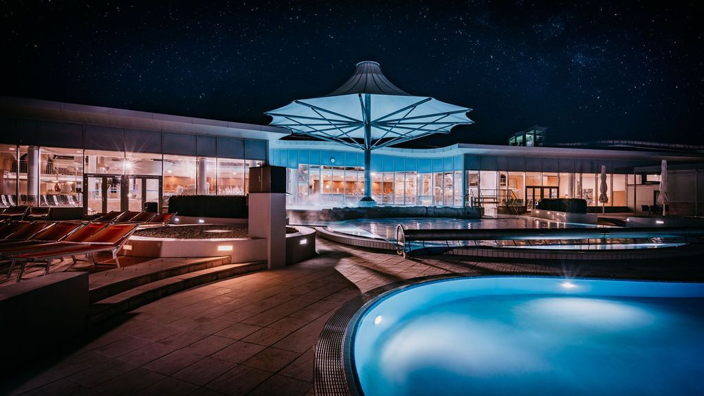 Night shot of a modern spa area with illuminated pools and a large parasol.