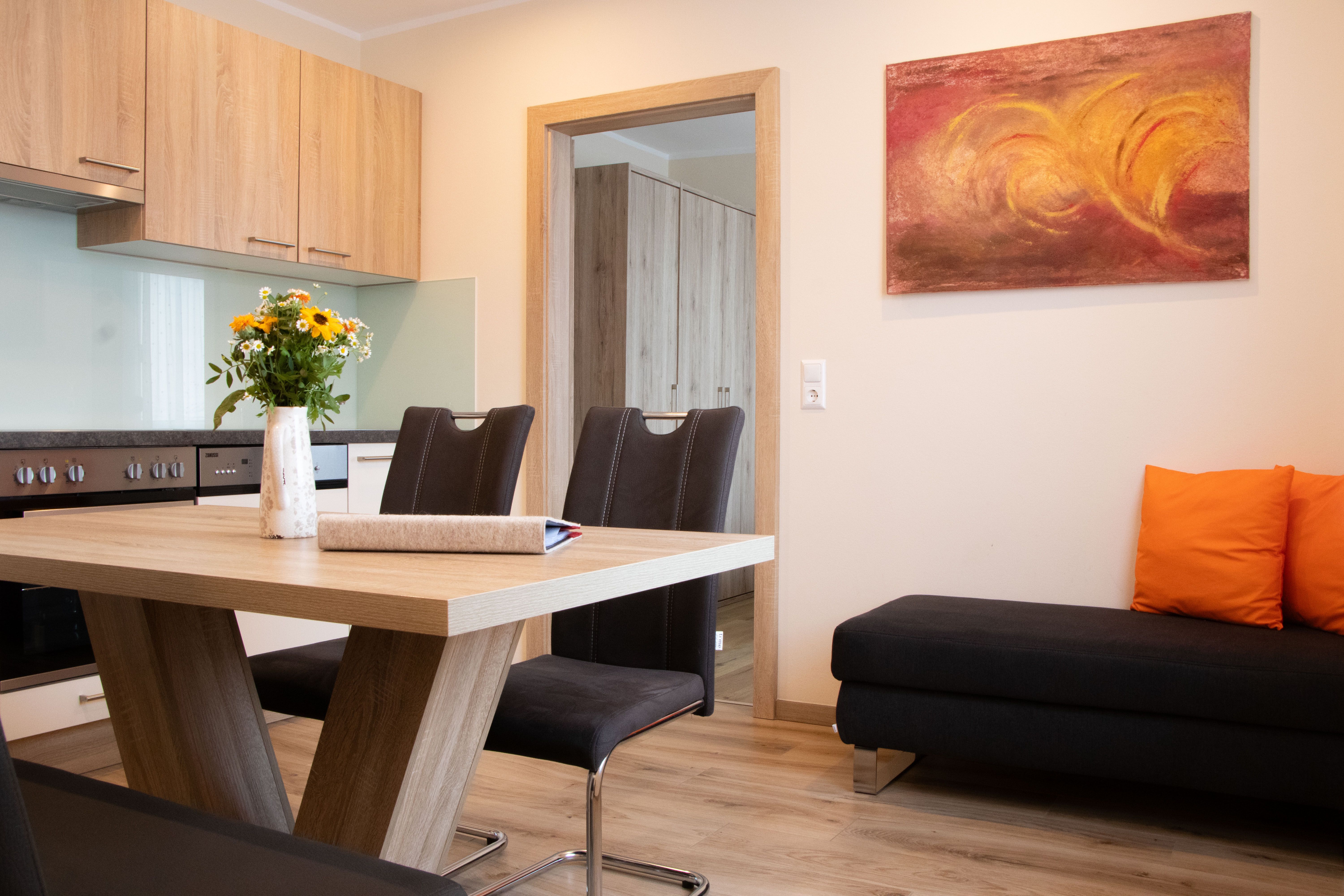 Moderne Küche mit Holzmöbeln, Esstisch, Stühlen und einem Sofa mit orangefarbenen Kissen.
