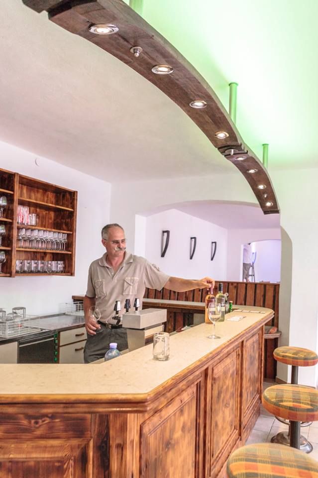 A man stands behind a wooden bar in a wine cellar and pours wine.